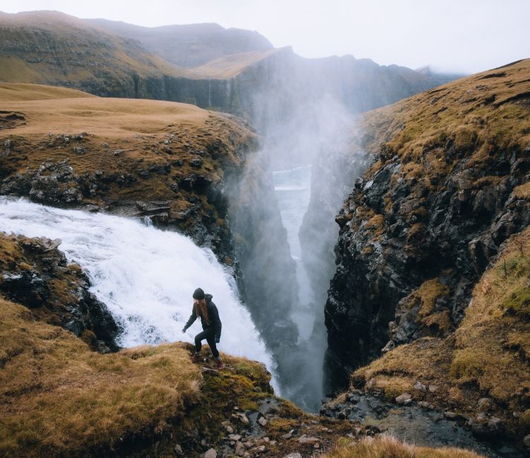 woman hiking next to waterfall into misty canyon